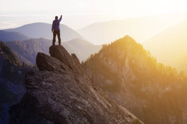 Dik bir kayalığın üstünde elleri havada maceraperest bir yürüyüşçü..
