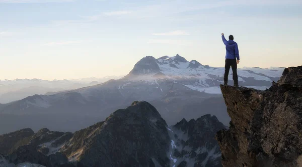 Kalandvágyó ember túrázó kezekkel a tetején egy meredek sziklás szikla. — Stock Fotó