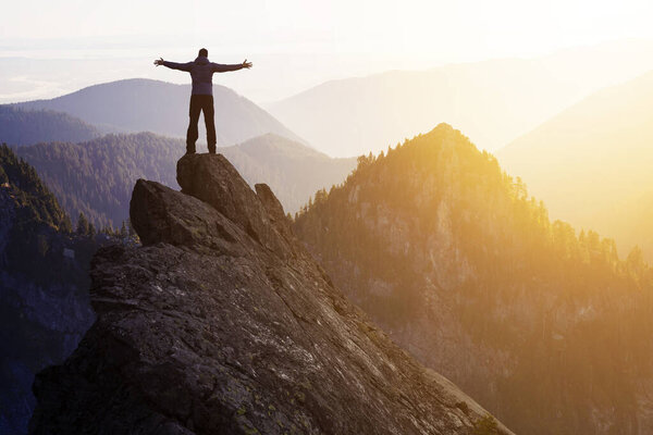Adventurous Man Hiker With Hands Up on top of a Steep Rocky Cliff.