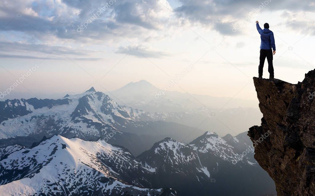 Adventurous Man Hiker With Hands Up on top of a Steep Rocky Cliff