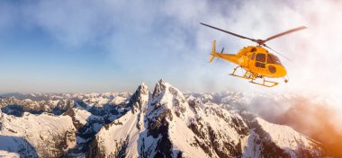 Sarı helikopter Rocky Dağları üzerinde uçuyor.