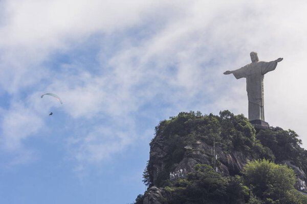 Летчик-парапланерист пролетает над статуей Кристо-Редентора на вершине Морро-ду-Корковадо, лес Тиджука, Рио-де-Жанейро, Бразилия
