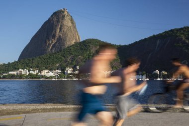 Okyanusun önünde bisiklet süren ve koşan erkeklerin güzel manzarası ve Sugar Loaf Dağı, Rio de Janeiro, Brezilya