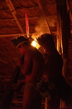 Amazon indigenous tribe playing traditional music instruments inside hut in the night, Amazonas, Brazil clipart