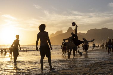 Ipanema Sahili 'nden Rio de Janeiro, Brezilya' da futbol oynayan insanlara güzel bir gün batımı manzarası