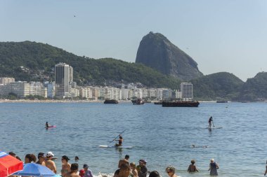 Copacabana Sahili 'ne güzel bir manzara. Arkasında Sugar Loaf dağı ve Stand Up Paddle tahtasındaki insanlar, Rio de Janeiro, Brezilya