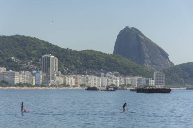 Copacabana Sahili 'ne güzel bir manzara. Arkasında Sugar Loaf dağı ve Stand Up Paddle tahtasındaki insanlar, Rio de Janeiro, Brezilya