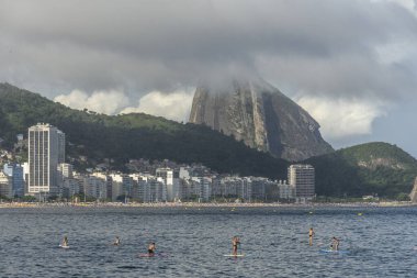Copacabana Sahili 'ne güzel bir manzara. Arkasında Sugar Loaf dağı ve Stand Up Paddle tahtasındaki insanlar, Rio de Janeiro, Brezilya