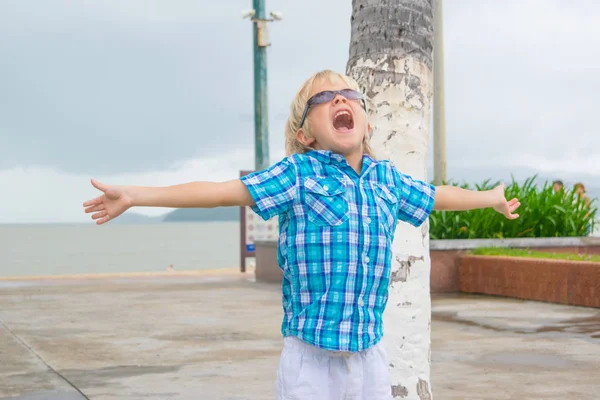 Een koele blonde jongen in zonnebril happyly schreeuwen in een park in de buurt van strand — Stockfoto