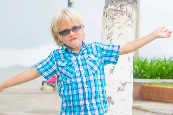 Ein cooler blonder Junge mit Sonnenbrille, der in einem Park spaziert — Stockfoto