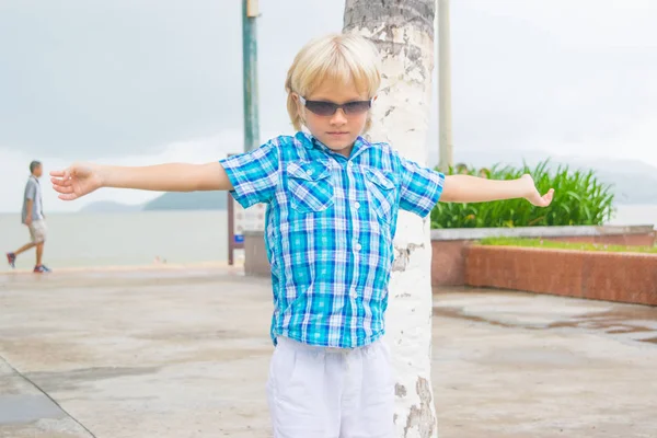Een koele blonde jongen in zonnebril wandelen in een park met armen opwaarts — Stockfoto