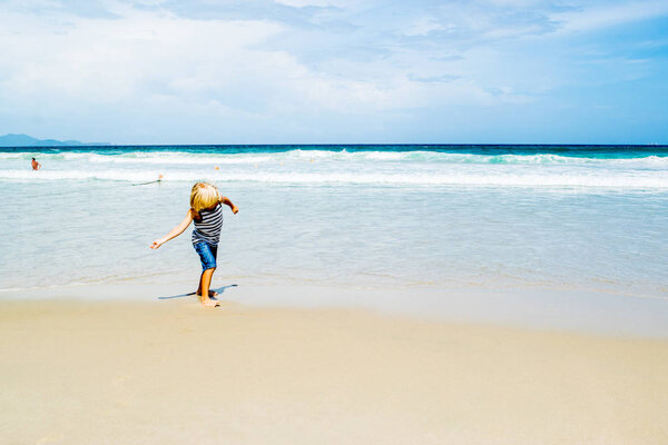 A blond boy (child) throwing a coin in water at a sea shore (beach), Nha Trang, Vietnam