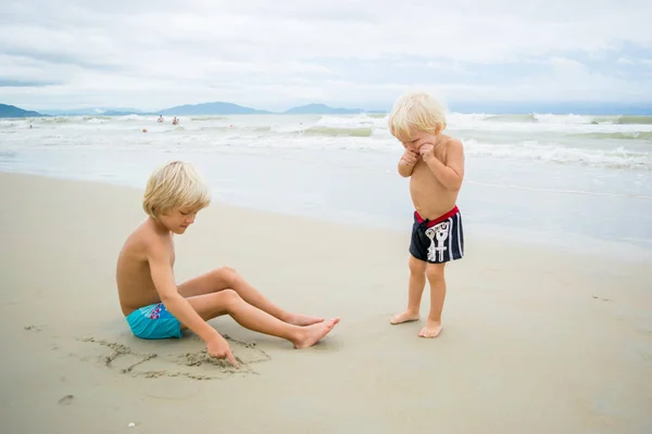 Zwei blonde Brüder spielen im Sand in der Nähe des Meerwassers am Strand — Stockfoto