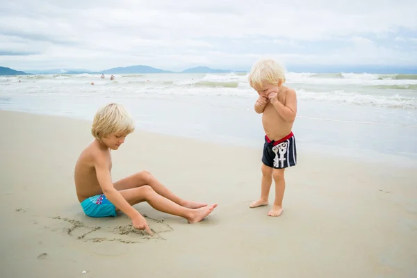 모래 해변에서 바다 물 근처에서 두 금발 형제 스톡 사진