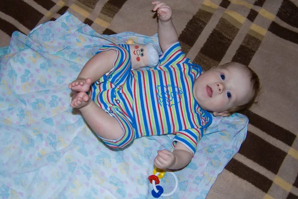 Gracioso bebé en una cama felizmente acostado en un azul rayas mamelucos — Foto de Stock