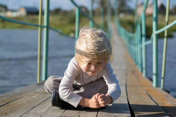 Ein glücklicher blonder Junge auf einer alten hölzernen Hängebrücke — Stockfoto