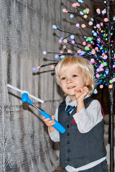 Garçon blond ludique près d'un arbre illuminé avec un jouet — Photo