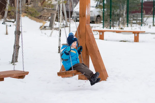 Niño feliz en columpios en un parque de invierno —  Fotos de Stock