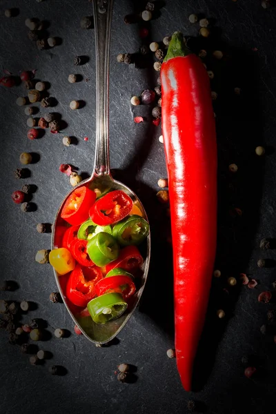 Peperoni au piment rouge avec poivre sur fond d'ardoise noire — Photo