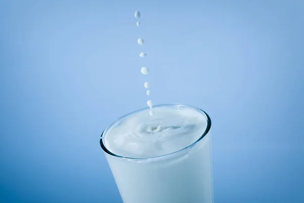 Verre à lait avec gouttes tombantes sur fond bleu — Photo