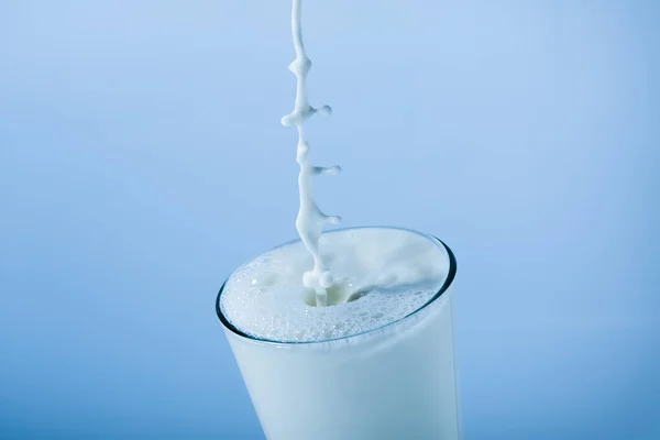 Ποτήρι γάλα βουτιά με πυλώνα σε μπλε φόντο — Φωτογραφία Αρχείου