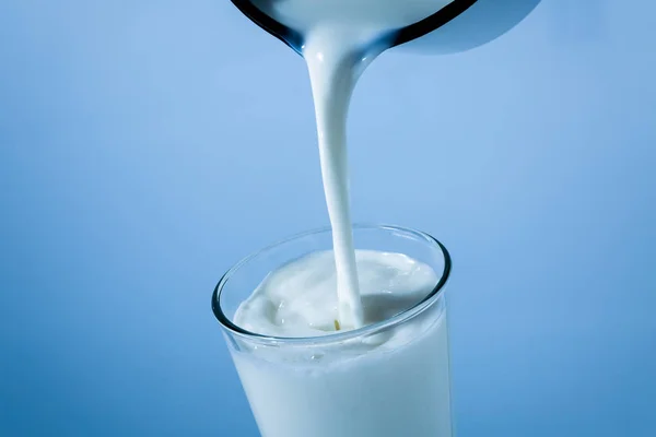 Verser le lait de la boîte de conserve dans un verre sur fond bleu — Photo