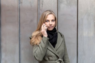 Smartphone metal duvar kullanarak ceket giyen genç kadın