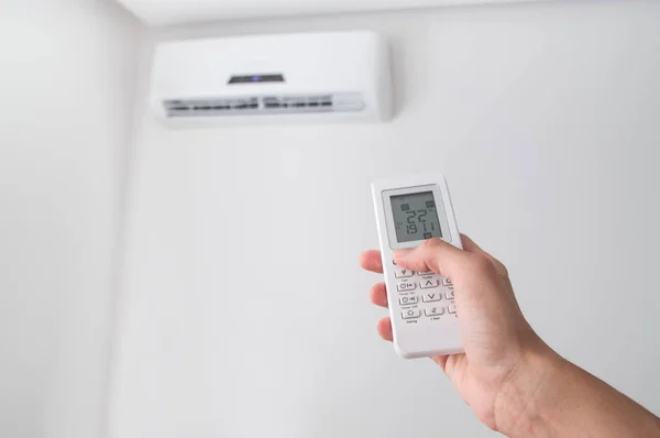 Hand met afstandsbediening voor air conditioner op de witte muur. — Stockfoto