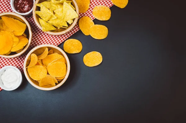 Aardappels, chips en snacks op zwarte leisteen tafel, bovenaanzicht — Stockfoto