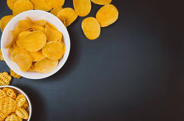 Aardappels, chips en snacks op zwarte leisteen tafel, bovenaanzicht — Stockfoto