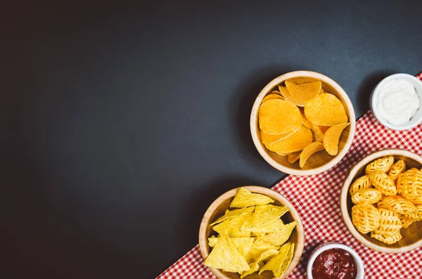 Potatischips och snacks på svart skiffer tabell, ovanifrån — Stockfoto