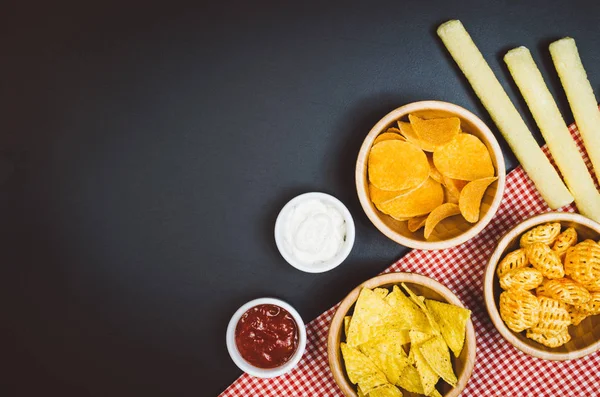 Aardappels, chips en snacks op zwarte leisteen tafel, bovenaanzicht — Stockfoto