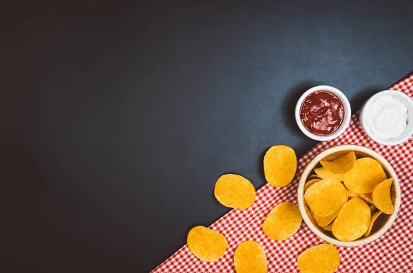 Batatas fritas e lanches na mesa de ardósia preta, vista superior — Fotografia de Stock