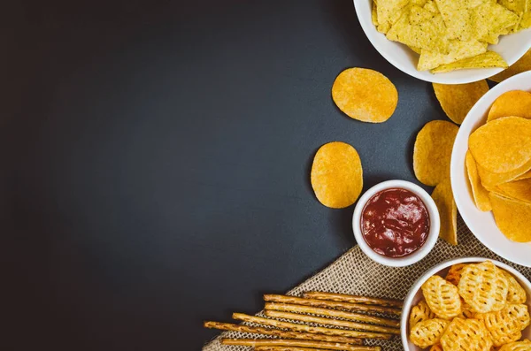 Aardappels, chips en snacks op zwarte leisteen tafel, bovenaanzicht — Stockfoto