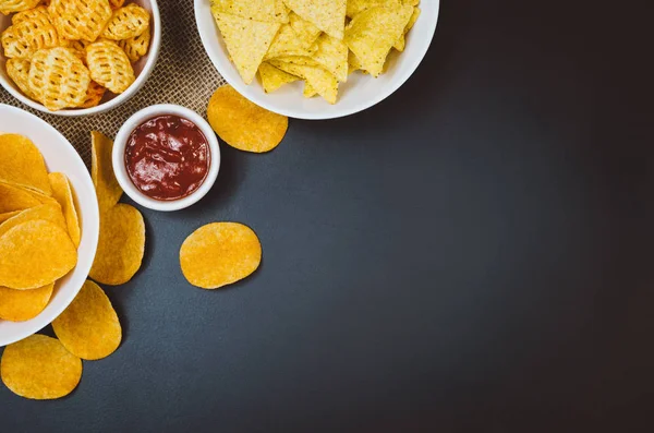Aardappels, chips en snacks op zwarte leisteen tafel, bovenaanzicht — Stockfoto