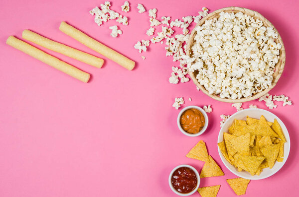 Попкорн и чипсы в миске на розовом фоне сверху
