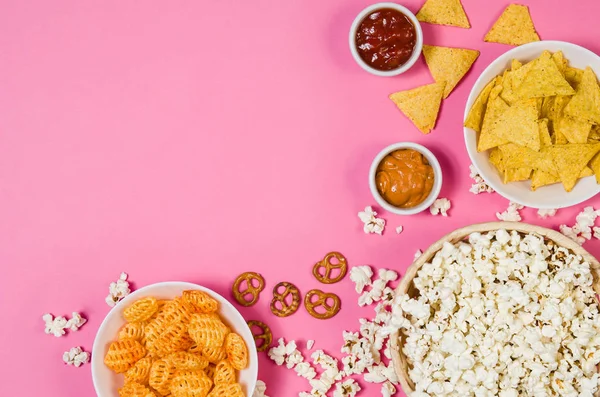 Popcorn und Chips in Schüssel auf rosa Hintergrund von oben — Stockfoto
