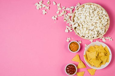 Popcorn and chips in bowl on pink background top view clipart