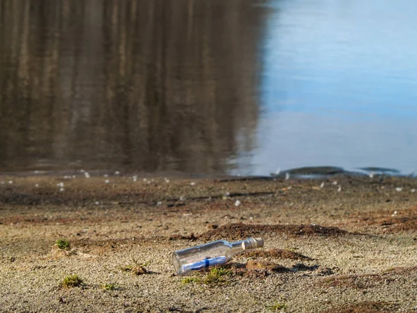 Mensaje en botella de cristal en la playa con agua y arena —  Fotos de Stock