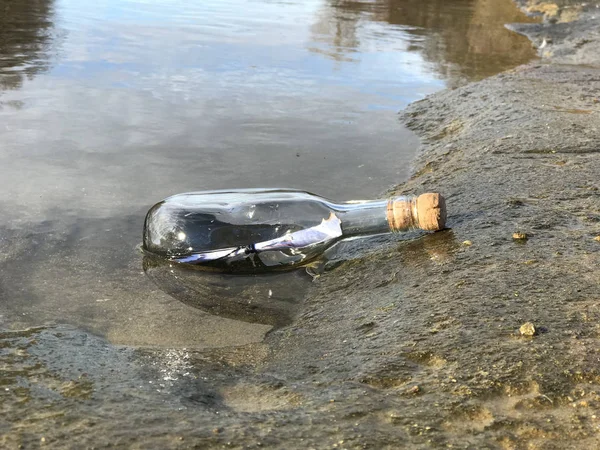 Mensagem em uma garrafa de cristal na praia com água e areia — Fotografia de Stock