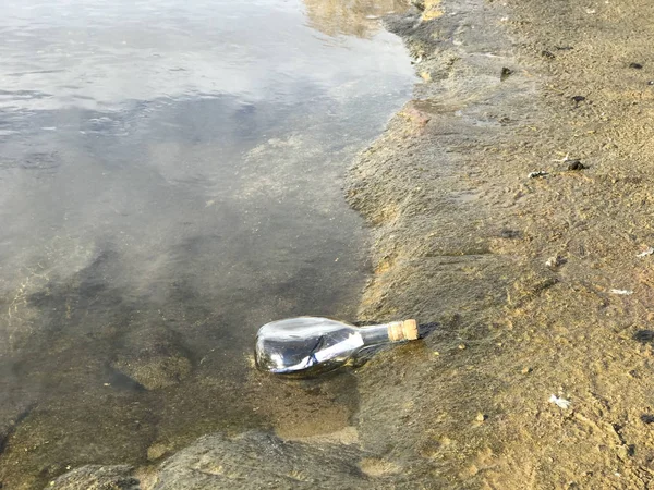 Mensaje en botella de cristal en la playa con agua y arena —  Fotos de Stock