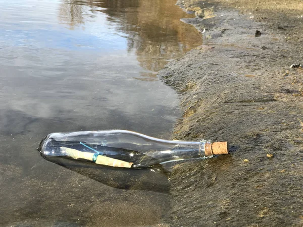 Mensaje en botella de cristal en la playa con agua y arena —  Fotos de Stock