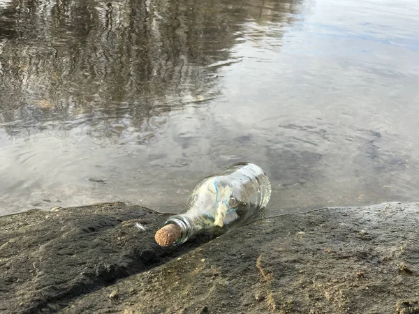 Mensaje en botella de cristal en la playa con agua y arena —  Fotos de Stock