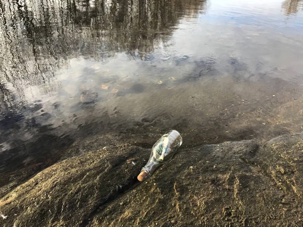 Mensagem em uma garrafa de cristal na praia com água e areia — Fotografia de Stock