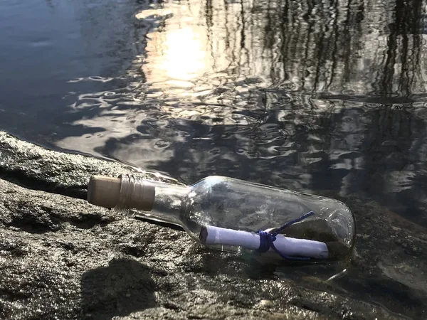 Mensaje en botella de cristal en la playa con reflejo de agua y arena y sol en el agua —  Fotos de Stock