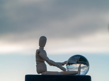 Wooden mannequin sitting with a crystal ball in his hands reflecting a landscape Ecology concept clipart