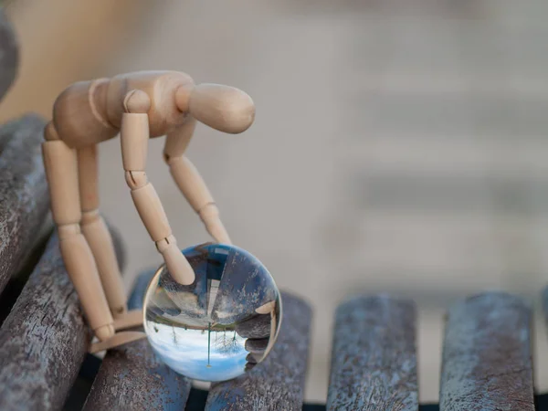 Crouching manichino in legno cattura con una palla di cristallo con le mani che riflette un concetto di ecologia paesaggio — Foto Stock