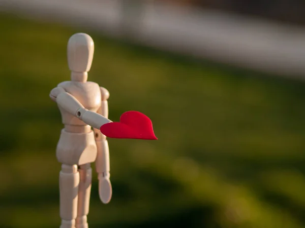 Houten mannequin met een rood hart op zijn handen Concept van romantiek en liefde — Stockfoto