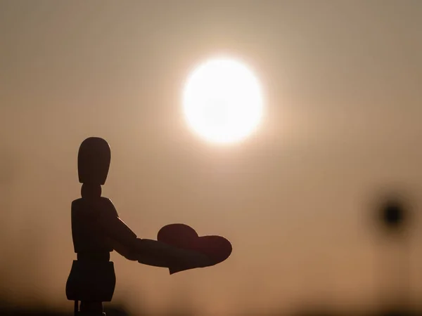 Wooden mannequin med et rødt hjerte på hænderne ved solnedgang Begrebet romantik og kærlighed - Stock-foto