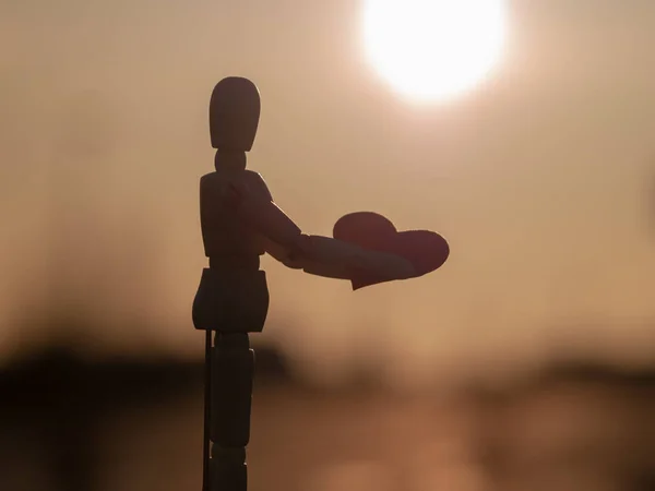 Деревянный манекен с красным сердцем на руках на закате концепция романтизма и любви — стоковое фото